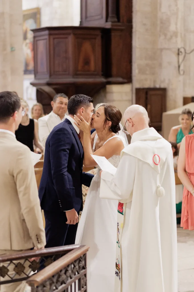 Couple de mariés s’embrassant devant le célébrant pendant leur cérémonie religieuse
