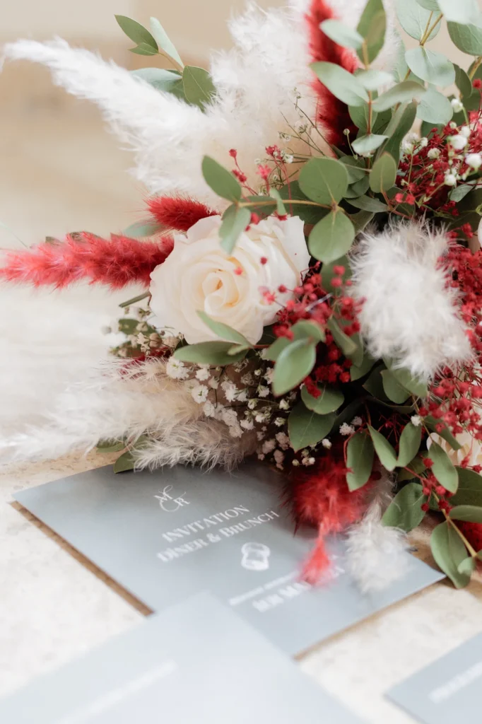 Bouquet de mariée de Mathilde aux tons blancs et rouges posé sur la papeterie du mariage