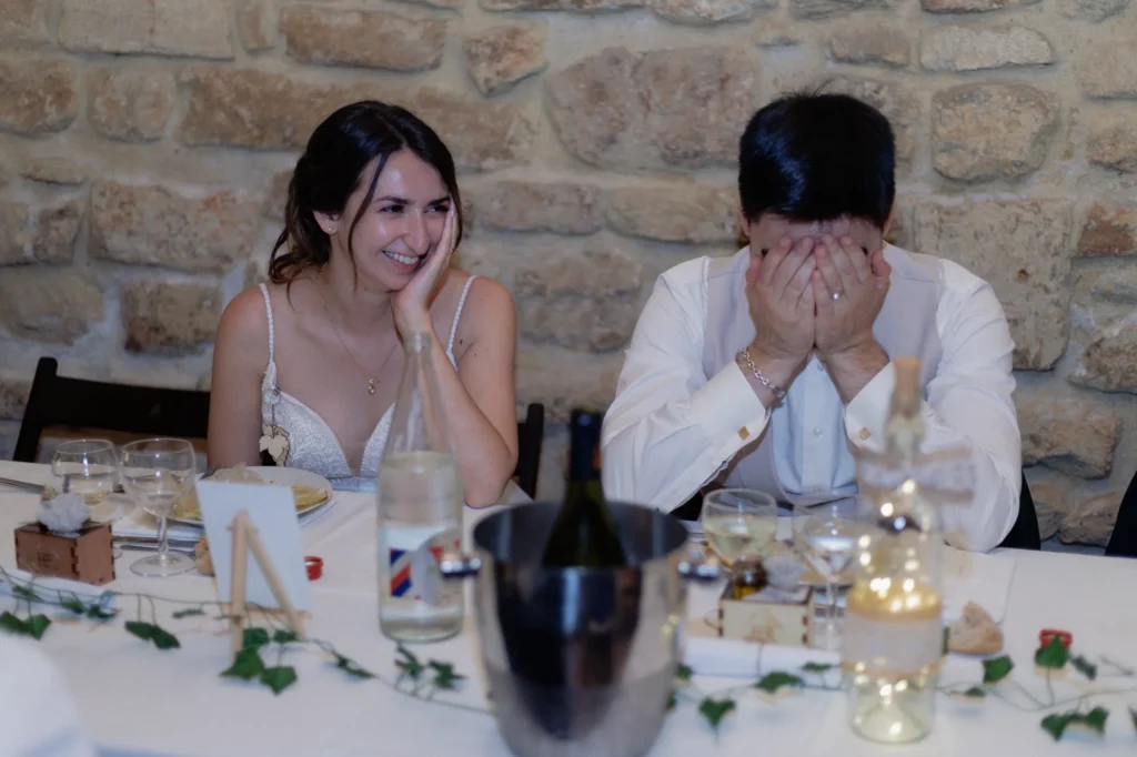 Mathilde sourit tandis que Romain cache son visage pendant un moment du dîner de mariage