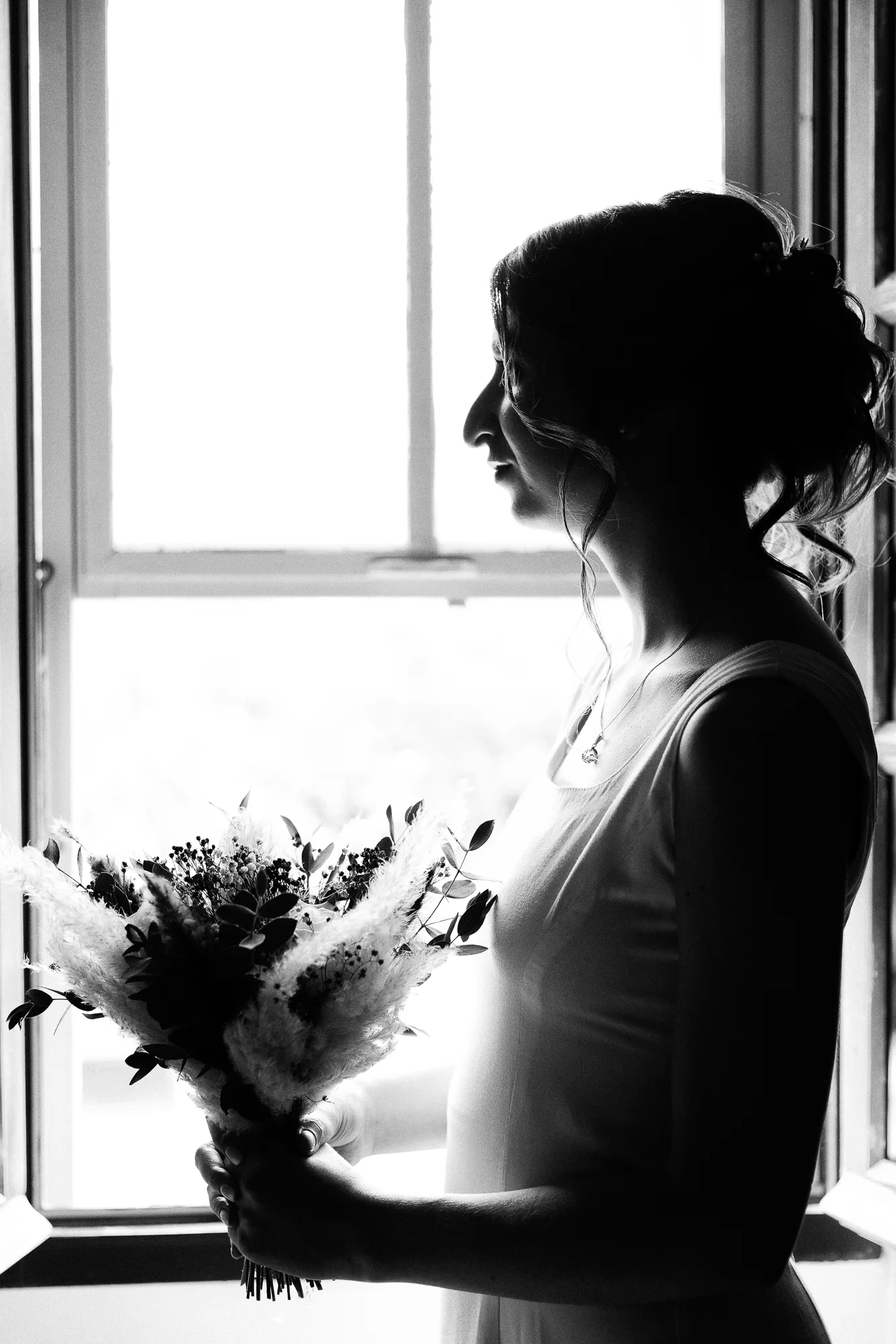 Silhouette en noir et blanc de Mathilde tenant son bouquet devant une fenêtre pendant les préparatifs